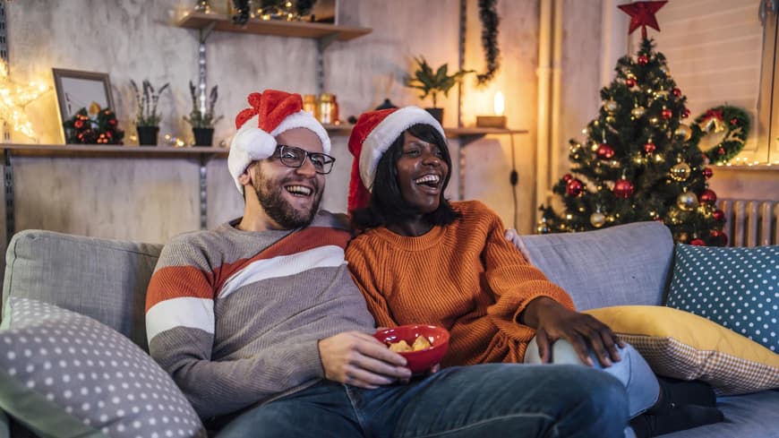 Romantische Weihnachtsfilme Netflix Glückliches Paar sitzt auf der Couch und guckt einen Weihnachtsfilm