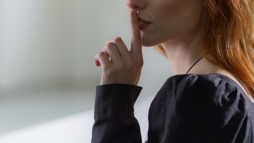 Schweigen statt Reden Frau hält ihren Zeigefinger vor ihren Lippen