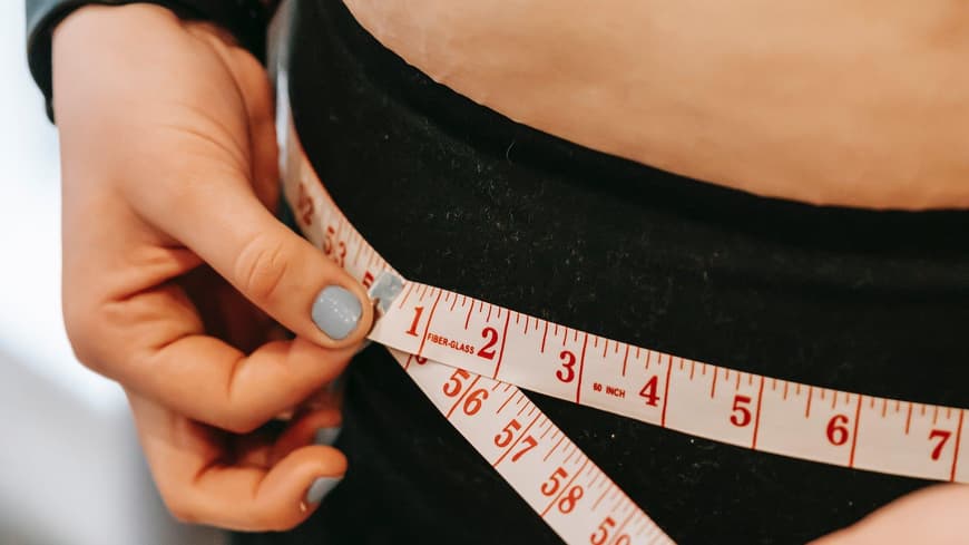 Frau mit Maßband misst den Bauchumfang.