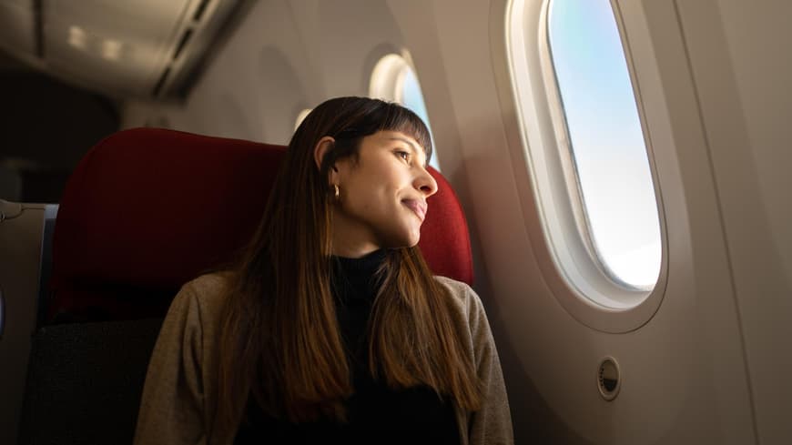 Darum solltest du keine Leggings ins Flugzeug tragen. Frau sitzt im Flugzeug und guckt aus dem Fenster
