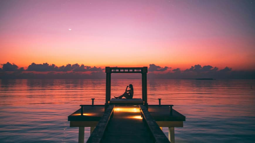 Wochenhoroskop Frau sitzt unter Sternenhimmel am Steg