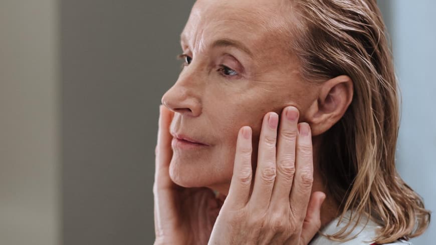 Das beste Serum ab 50 sollte viel Feuchtigkeit spenden. Ältere Frau fasst sich mit den Händen ins Gesicht.