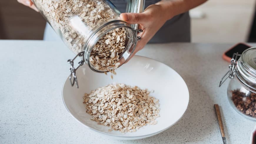 Abnehmen mit Haferflocken kann für viele Menschen hilfreich sein. Eine Person schüttet Haferflocken aus einem Glasgefäß in eine Schüssel.