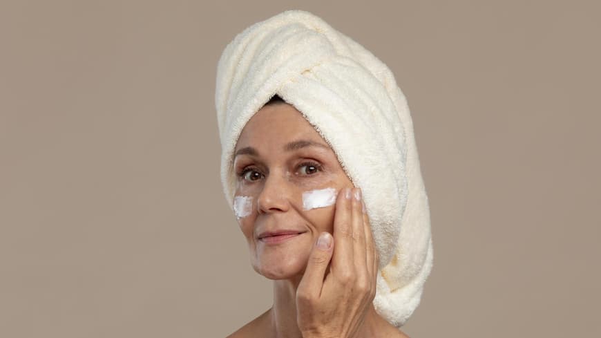 Die besten Gesichtscremes aus der Apotheke für reife Haut zeigen wir dir hier. Frau cremt sich ihr Gesicht ein.