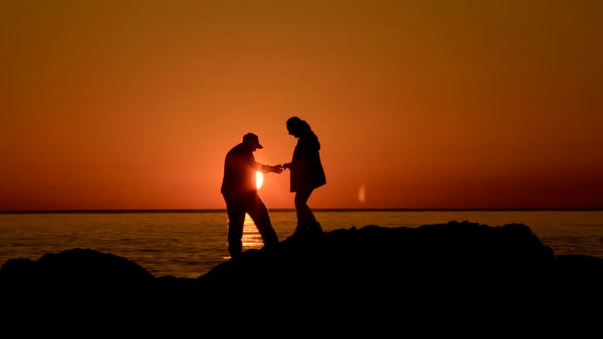 An diesen Anzeichen erkennt man gute Menschen. Mann hilft Frau über Steine zu gehen