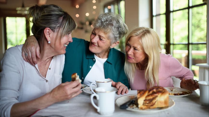 Gerade in größerer Runde wird man schnell zum Lästern verleitet. Drei Frauen sitzen am Tisch und sprechen und essen Kuchen.