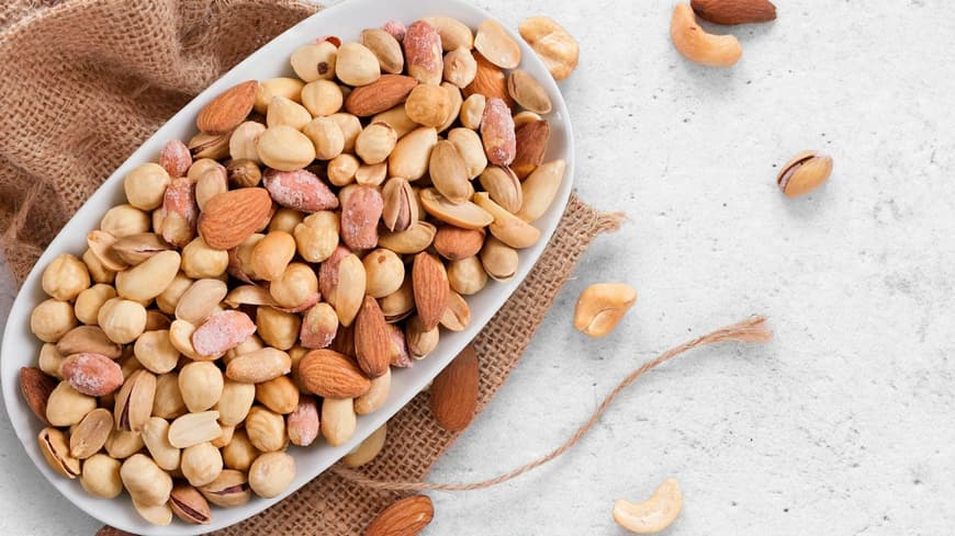 Abnehmen mit Nüssen kann gelingen, wenn man ein paar Dinge beachtet. Verschiedene Nüsse in einer weißen Schale, die auf einem braunen Jutebeutel steht.
