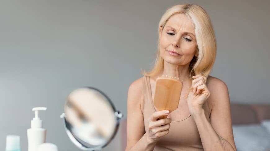 Bei Haarausfall sollten wir laut Expertin täglich Haarewaschen – aus DIESEM Grund. Reife Frau bürstet Haare kritisch