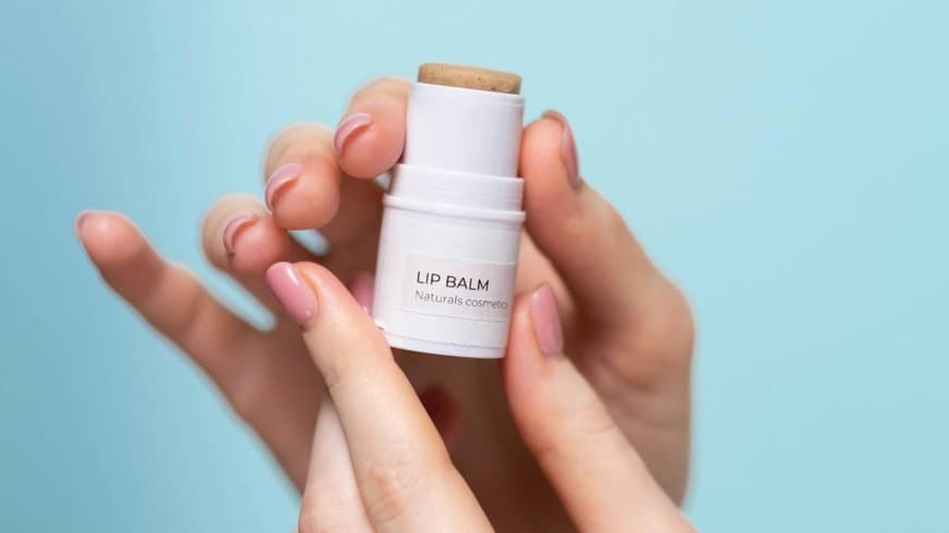 Peptide Lip Balms sind ein angesagter Beauty-Trend. Ein Lip Balm wird in der Hand vor einem hellblauen Hintergrund gehalten.