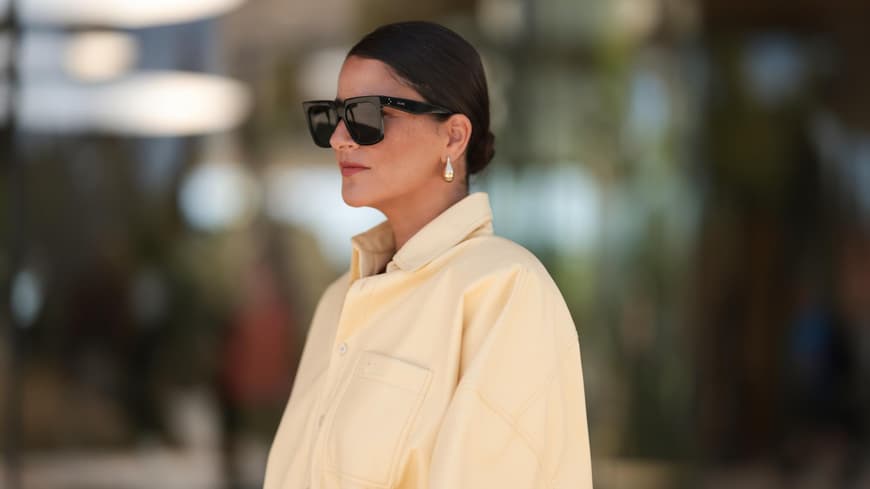 Ein Dutt mit kurzen Haaren wirkt edel und ist praktisch zugleich. Frau mit einer gelben Jeansbluse, Sonnenbrille und einem niedrigen Dutt mit kurzen Haaren.