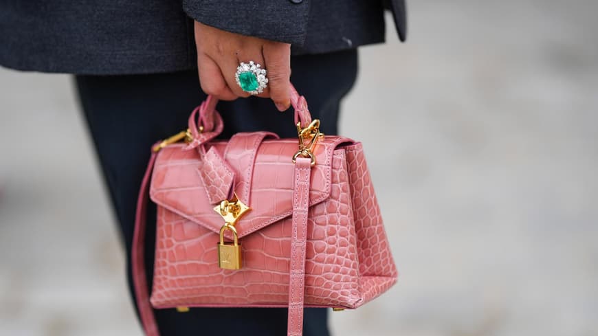 Edelstein-Schmuck in allen möglichen Formen ist wieder im Trend. Eine kleine rosane Tasche wird von einer Hand mit einem Smaragd-Ring gehalten.