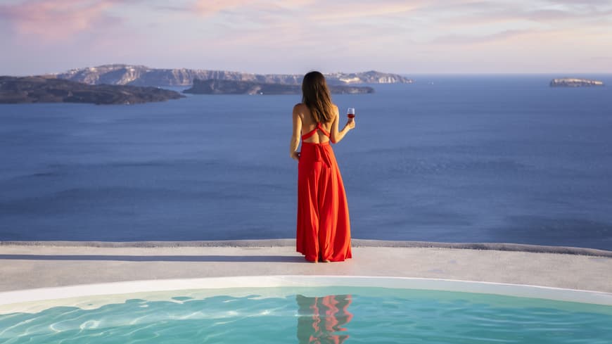 Dieses elegante Maxikleid von H&M versetzt uns sofort in Luxus-Urlaubsstimmung. Frau steht in rotem Kleid am Pool und blickt aufs Meer.