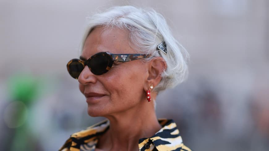 Welches Make-up bei heißem Wetter eine gute Wahl ist, kann eine wichtige Frage am Morgen sein. Frau mit grauen kurzen Haaren, einer Sonnenbrille und einem getigerten Oberteil guckt zur Seite.