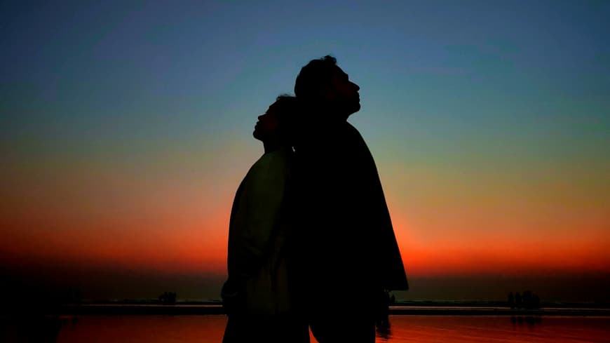 Welchen 4 Sternzeichen die intensivste Verbindung ihres Lebens bevorsteht? Das erfährst du hier. Ein Paar steht Rücken an Rücken vor dem Nachthimmel.