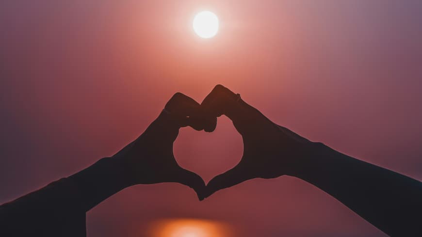 Welche Sternzeichen im Juli großes Liebesglück erwartet, erfährst du hier. Hände formen ein Herz vor dem Abendhimmel