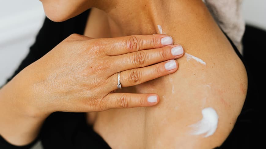 Retinol Bodylotions können unsere Haut am Körper genauso frisch und jung halten, wie Cremes für das Gesicht. Frau cremt Schulter ein