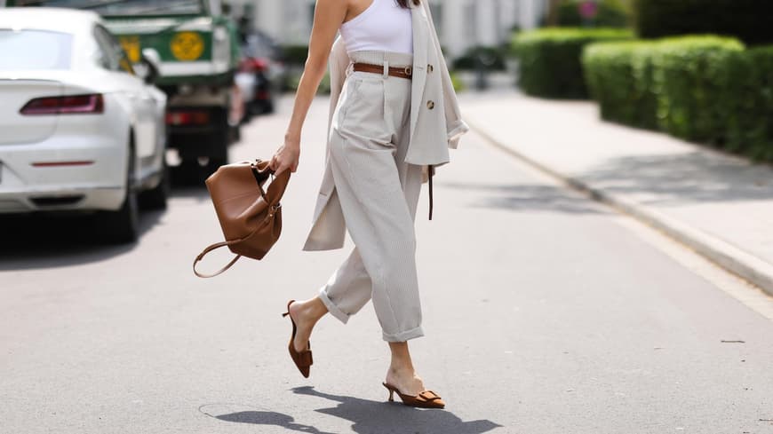 Sommerschuhe wie Kitten Heels sind Trend 2025. Frau mit rotem Lippenstift trägt ein weißes Top, eine beige Chinohose und Kitten Heals auf der Straße.