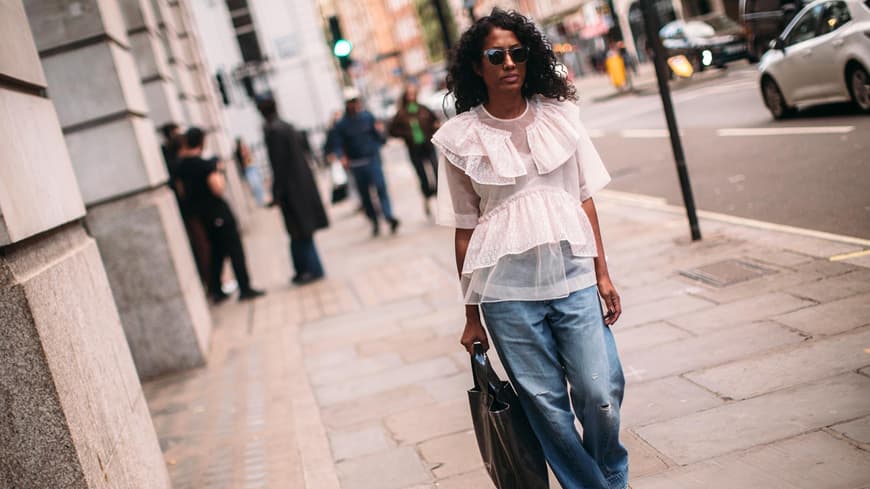 Eine Frau mit Baggy Jeans und weißer Bluse mit Volants