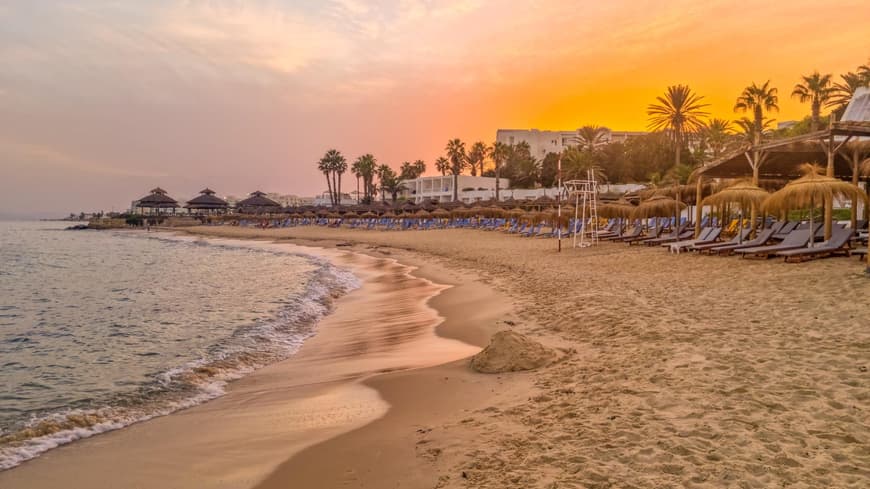 In Hammamet lässt sich herrlich der Tag am Strand ausklingen. Ein Strand bei Sonnenuntergang in Tunesien mit Liegen und Schirmen.