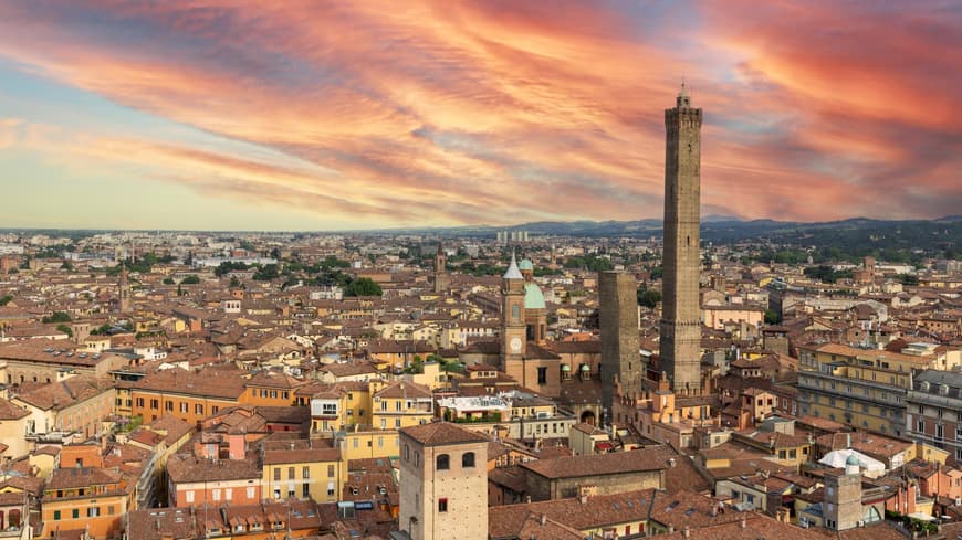 Bologna ist eine Stadt in Italien, die mit Gastronomie, Historie und Charme überzeugt. Ein Blick über die Dächer von Bologna bei einem rötlichen Himmel.
