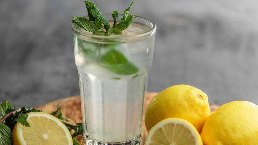 Schlankwasser soll beim Abnehmen helfen. Ein großes Glas mit Wasser und frischer Minze drin, drum herum liegen aufgeschnittene Zitronen.