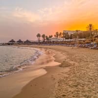 In Hammamet lässt sich herrlich der Tag am Strand ausklingen. Ein Strand bei Sonnenuntergang in Tunesien mit Liegen und Schirmen.