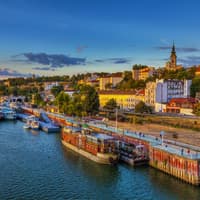 Belgrad ist eine Hafenstadt, die viel mehr zu bieten hat, als viele denken. Ein Blick über den Hafen von Belgrad mit Schiffen im Wasser und Häusern an Land, die von der Sonne beleuchtet werden.