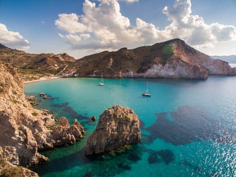 Die Buchten an der Insel Milos sprühen eine besondere Ruhe aus. Das Meer an der Küste der Insel Milos mit zwei Segelbooten drauf.