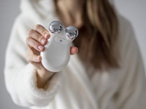 Die besten Gesichtsmassagegeräte gegen Falten findet man gar nicht so leicht. Frau hält ein Mikrostromgerät zur Massage des Gesichts in ihren Händen