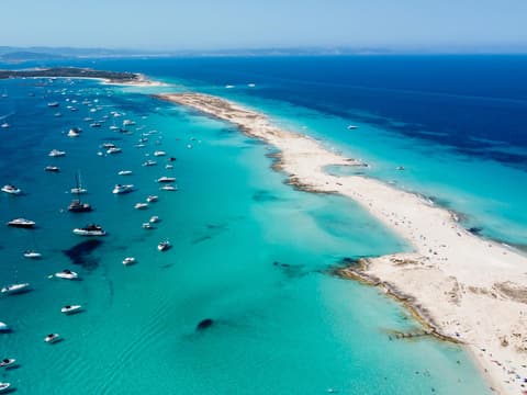 Formentera glänzt mit einem atemberaubenden Strand. Ein langer Sandstrand mit türkisblauem Meer und Yachten darin.