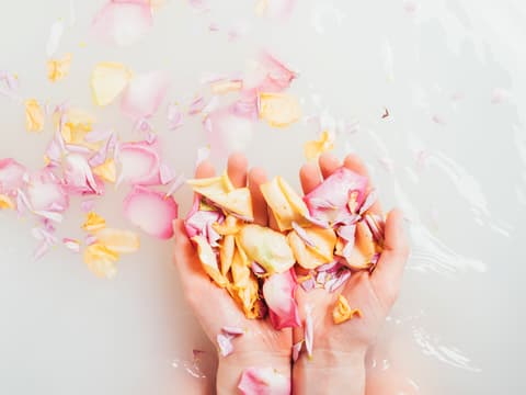 Diese blumigen Drogerie-Duschgele duften nach Frühling. Frau streut Blütenblätter ins Badewasser.