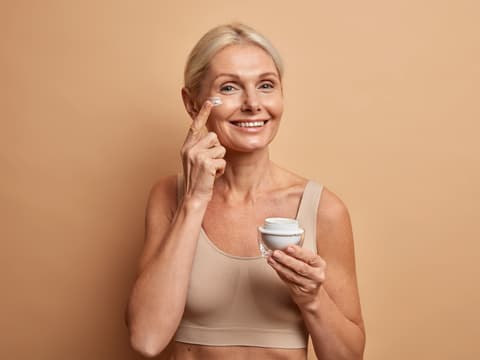 Die optimale Gesichtspflege ab 60? Wir haben die wichtigsten Tipps. Ältere Frau cremt sich das Gesicht ein.