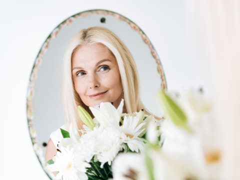 Wie du einen Grünstich mit Hausmitteln entfernen kannst, erfährst du hier. Blonde Frau schaut in den Spiegel