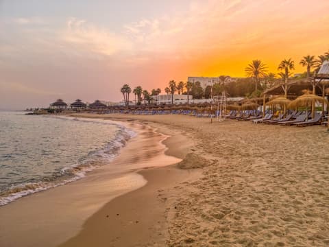 In Hammamet lässt sich herrlich der Tag am Strand ausklingen. Ein Strand bei Sonnenuntergang in Tunesien mit Liegen und Schirmen.