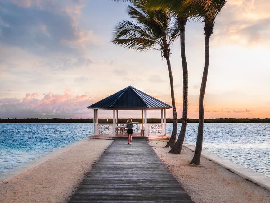 Reisetipps findest du hier zu Genüge. Frau läuft auf einem langen Steg unter Palmen auf einen Pavillon am Meer zu.
