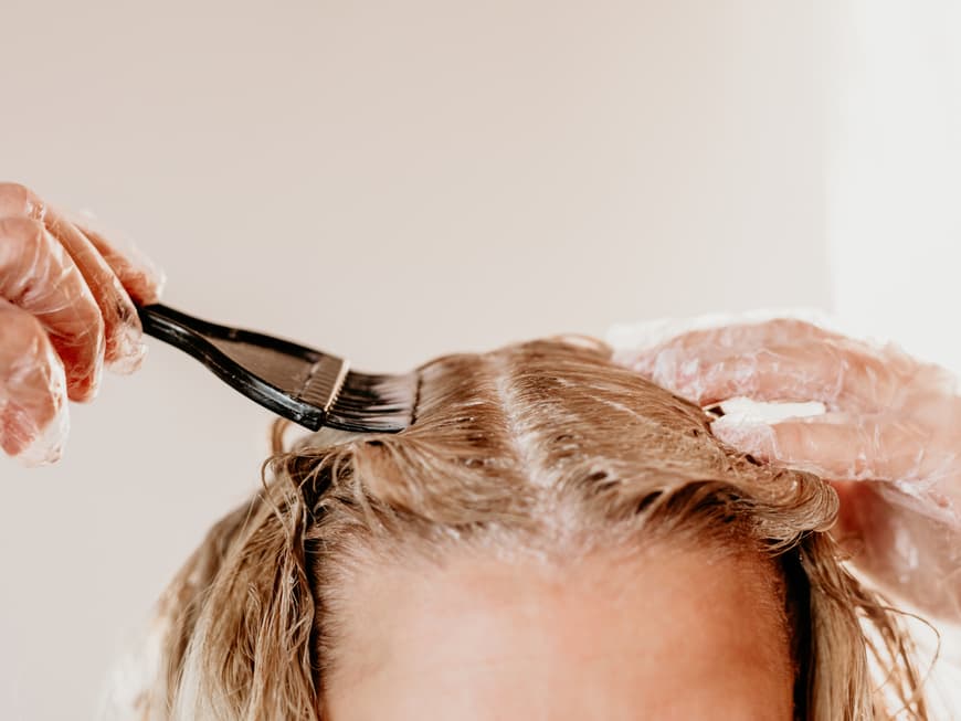 Beim Selberfärben kann es schnell mal zu einem unerwünschten Grünstich kommen. Frau färbt Haare blond.