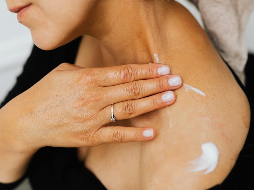 Retinol Bodylotions können unsere Haut am Körper genauso frisch und jung halten, wie Cremes für das Gesicht. Frau cremt Schulter ein