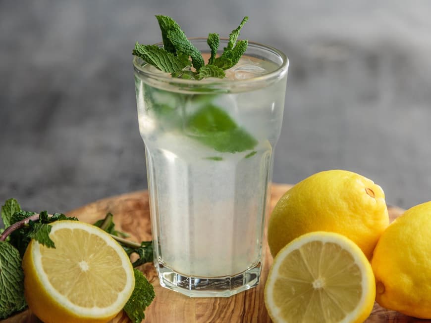 Schlankwasser soll beim Abnehmen helfen. Ein großes Glas mit Wasser und frischer Minze drin, drum herum liegen aufgeschnittene Zitronen.